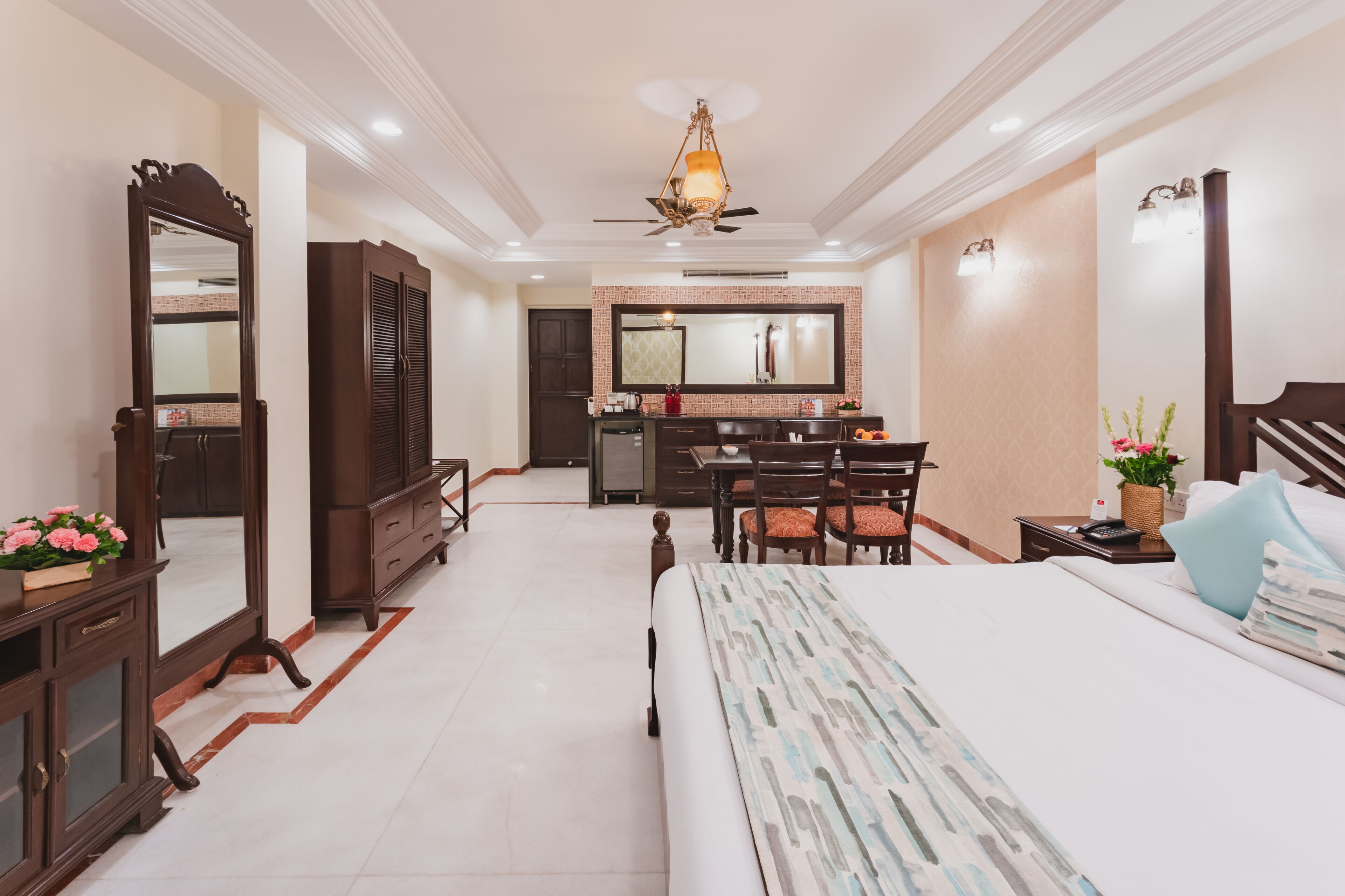 A hotel room with a bed, a desk, a chair, a dresser, a mirror, a ceiling fan, and a bathroom with a sink and mirror.