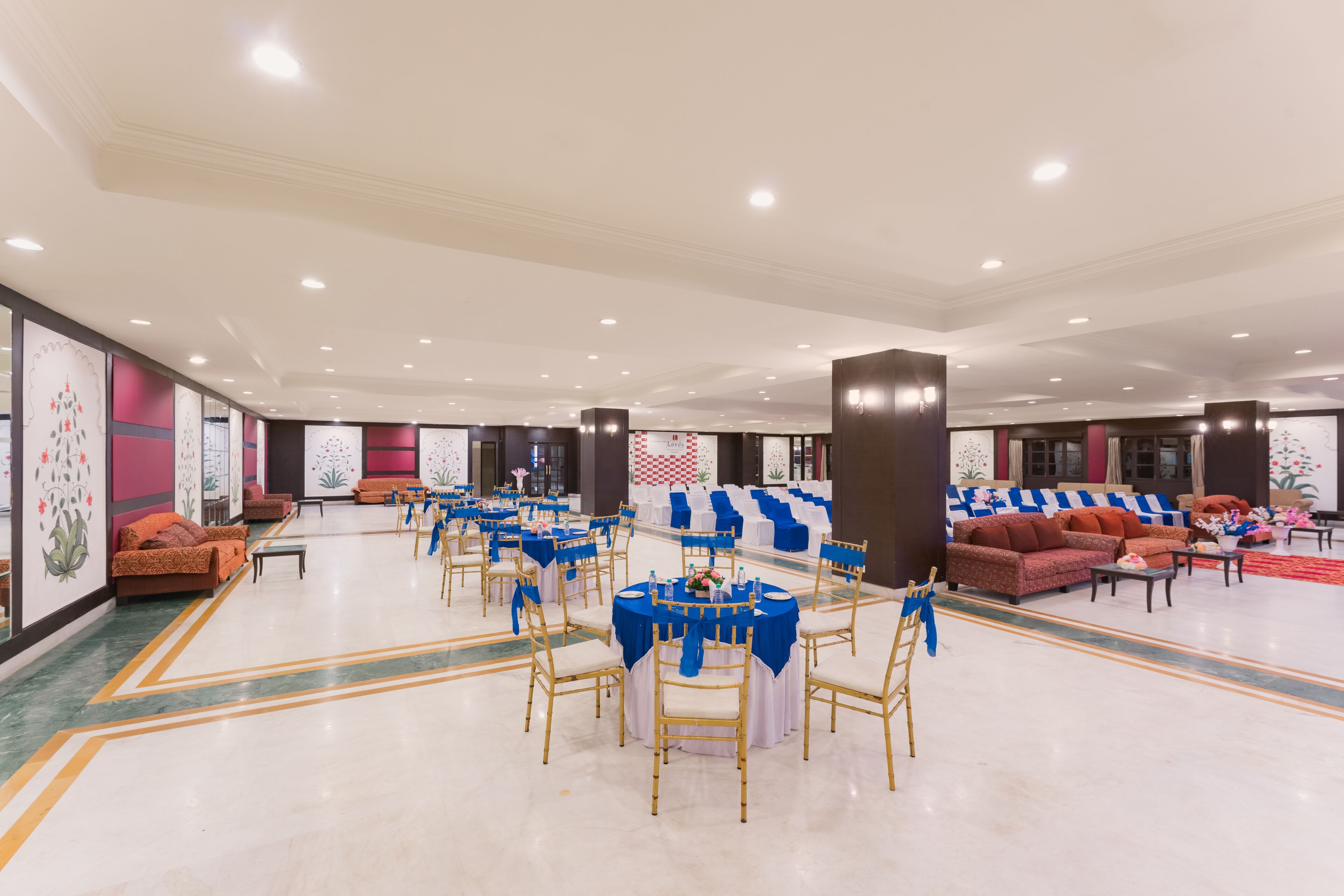 A spacious banquet hall with round tables, blue tablecloths, and gold chairs.