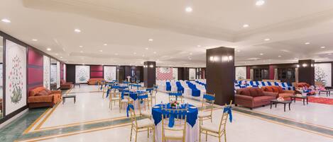 A spacious banquet hall with round tables, blue tablecloths, and gold chairs.