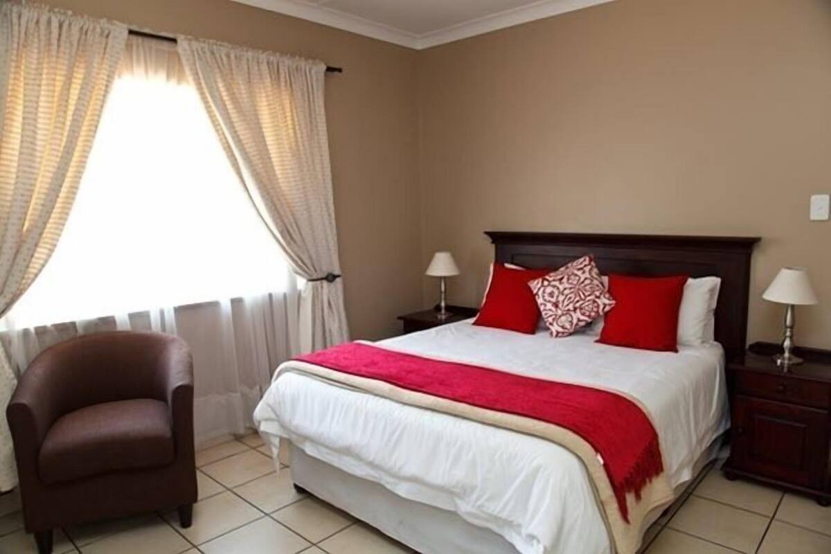 A hotel room with a bed, two bedside tables, a chair, and a window with curtains.