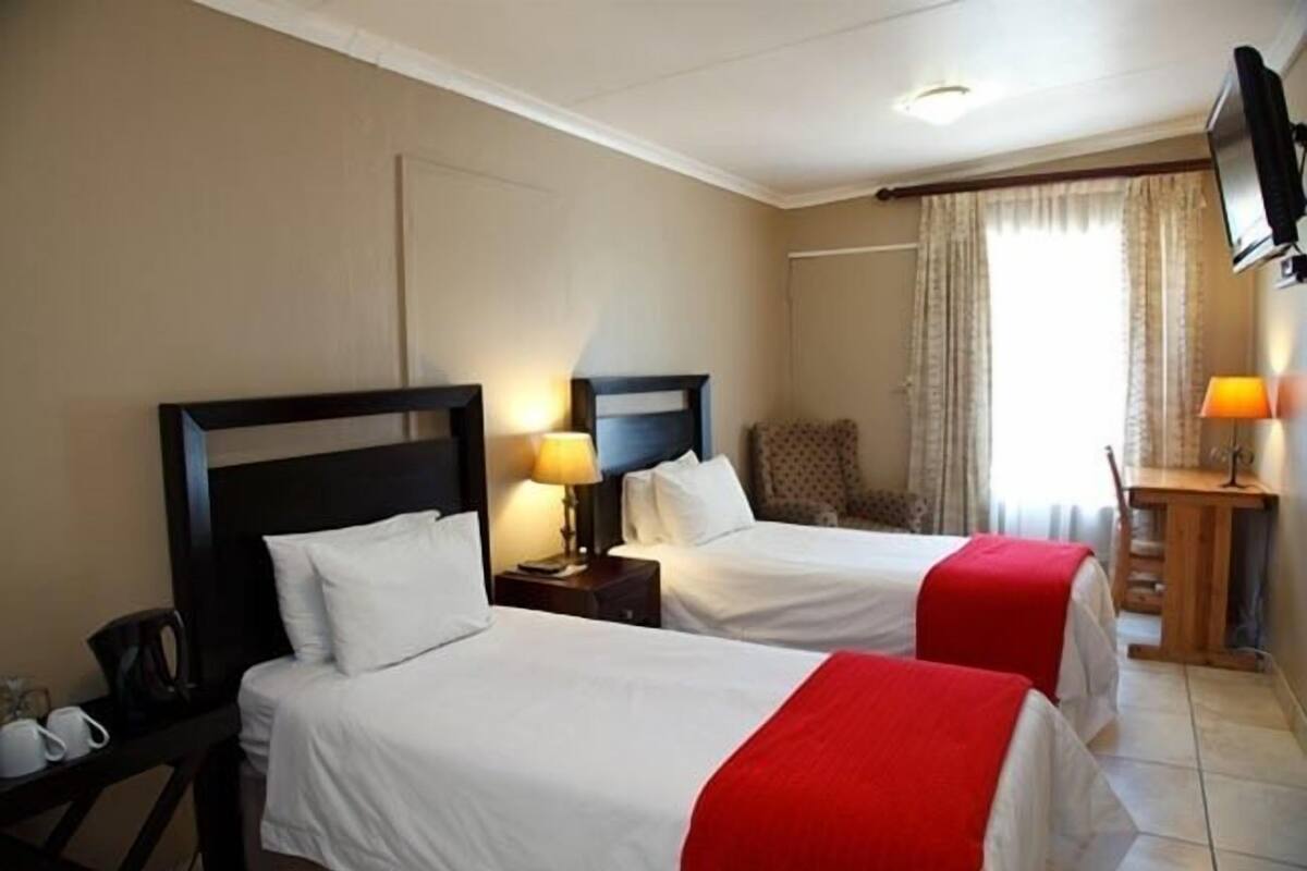 A hotel room with two beds, a TV, a desk with a lamp, and a window with curtains.