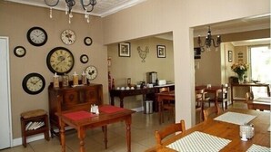 Un comedor con mesas y sillas de madera, una araña y varios relojes de pared.