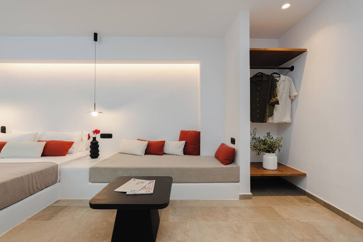 A modern hotel room with a sofa bed, a small table, a hanging coat rack, and a potted plant.