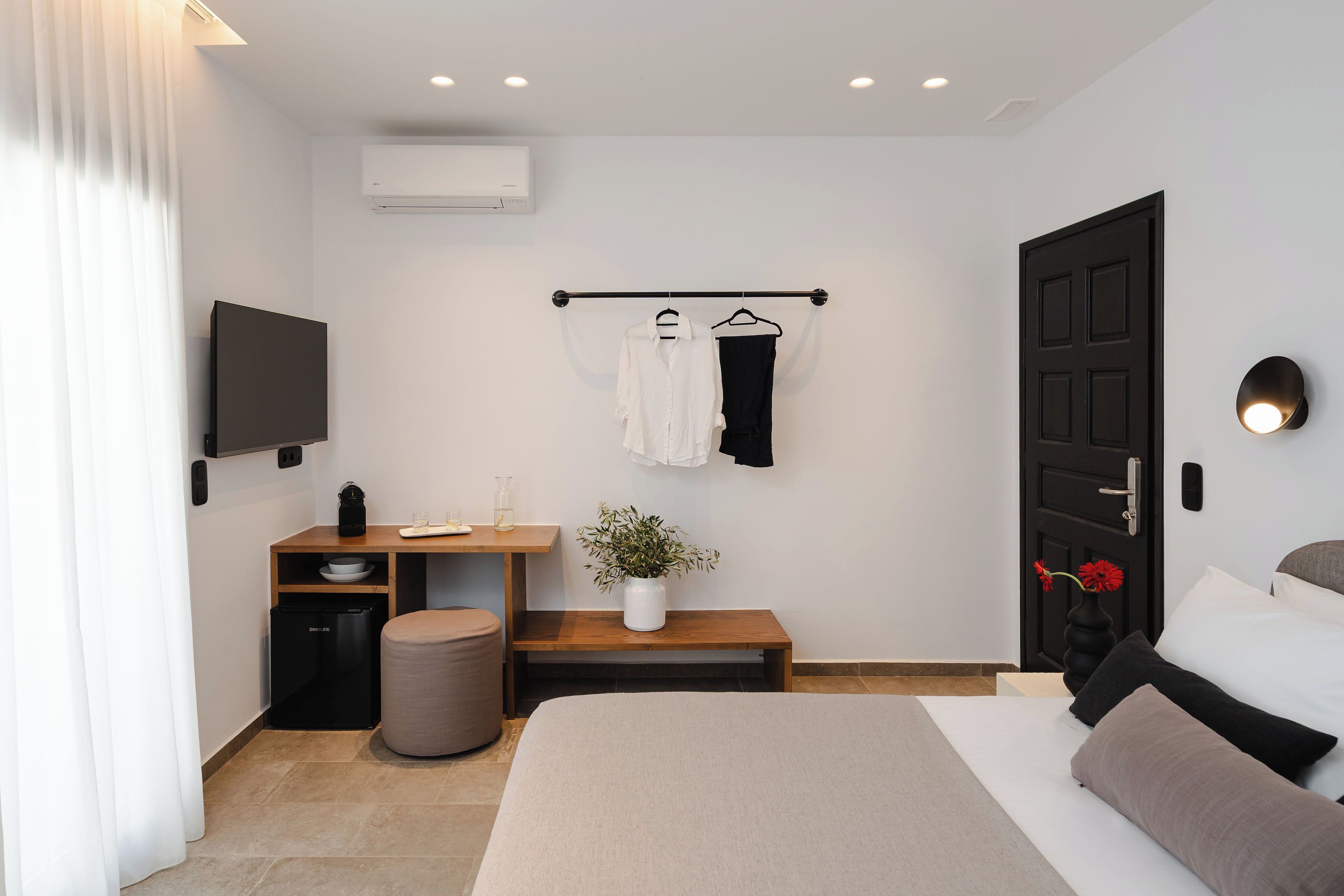 Ein modernes Hotelzimmer mit Bett, Nachttisch, Fernseher und einer kleinen Küchenzeile.