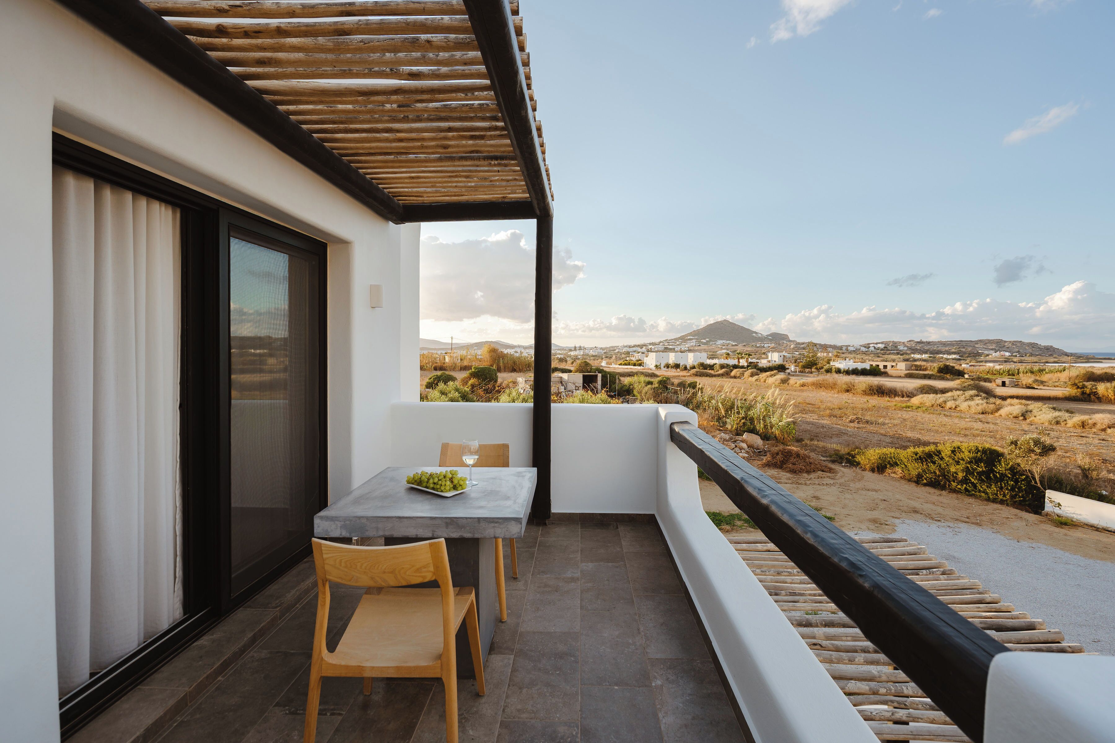 A balcony with a table and chairs, a view of the countryside, and a wooden pergola.