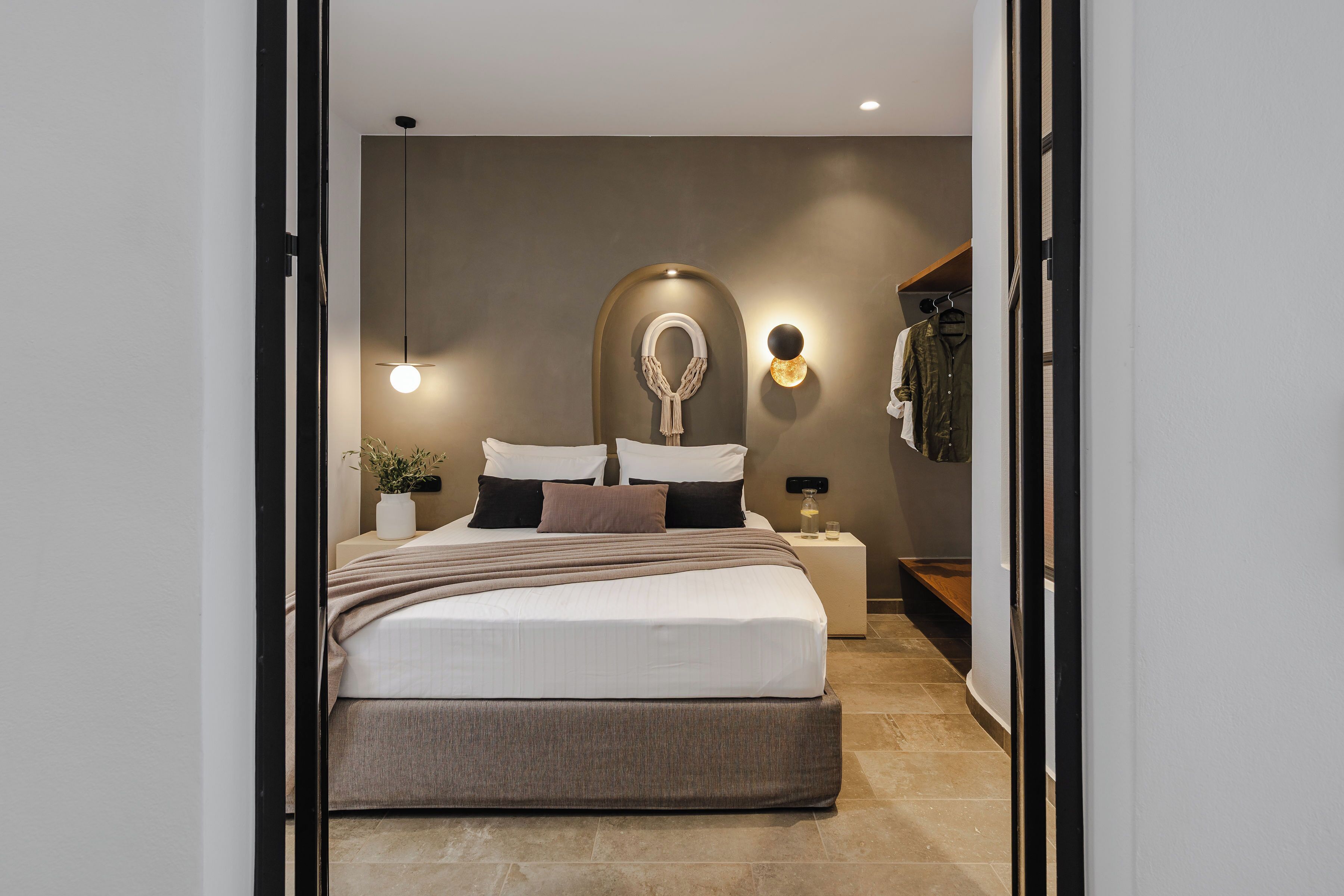 A modern bedroom with a large bed, bedside tables, a mirror, and a hanging coat rack.