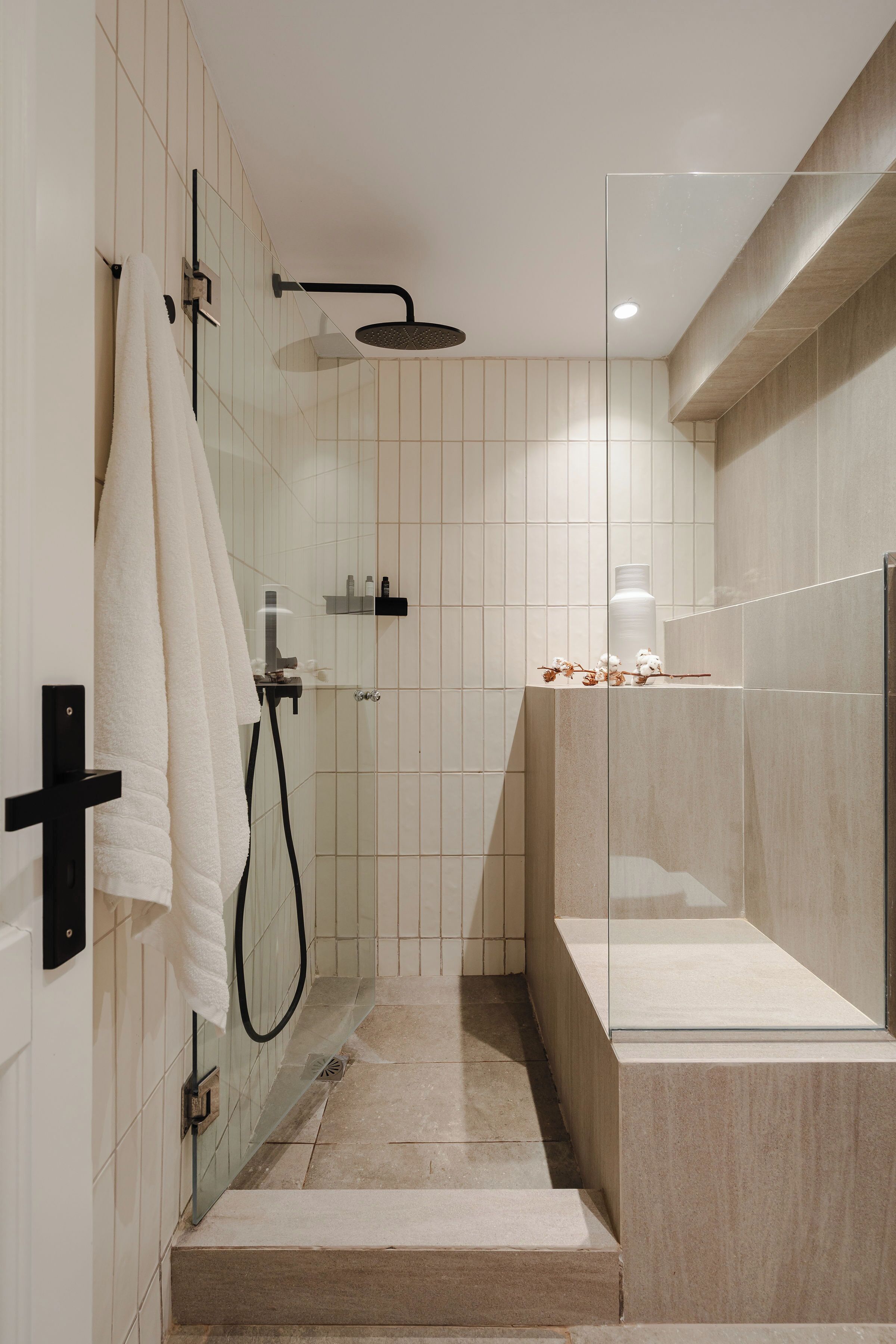 A modern shower area with a glass enclosure, a towel rack, and a shelf with toiletries.