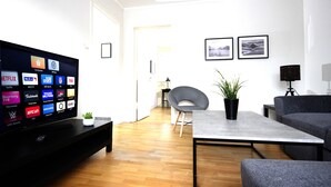 Una sala de estar moderna con una televisión de pantalla plana mostrando varias aplicaciones de transmisión, un sillón gris, una mesa de centro con una planta y un sofá gris.