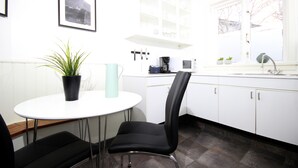 Una cocina moderna con armarios blancos, una silla negra, una mesa blanca y una planta en maceta.