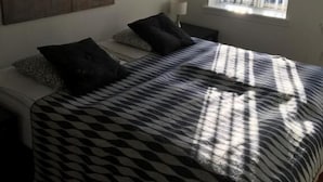 Un dormitorio con cama, almohadas, un reloj de pared, una ventana y una lámpara.