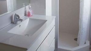 Un baño con lavamanos blanco, un espejo y zona de ducha.