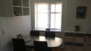 Una habitación con una mesa redonda y cuatro sillas, una ventana con persianas, un radiador y una estantería con objetos.