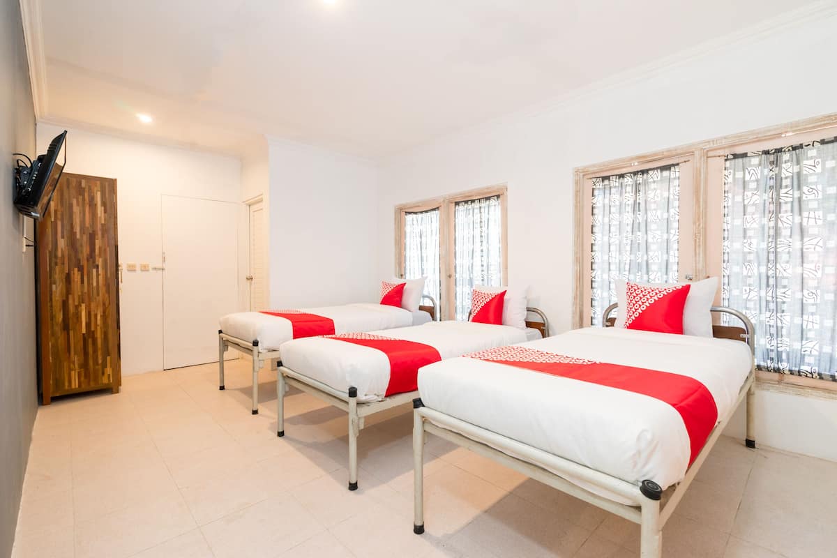 A hotel room with three beds, each with white bedding and red accents, a wooden panel wall, and a door.