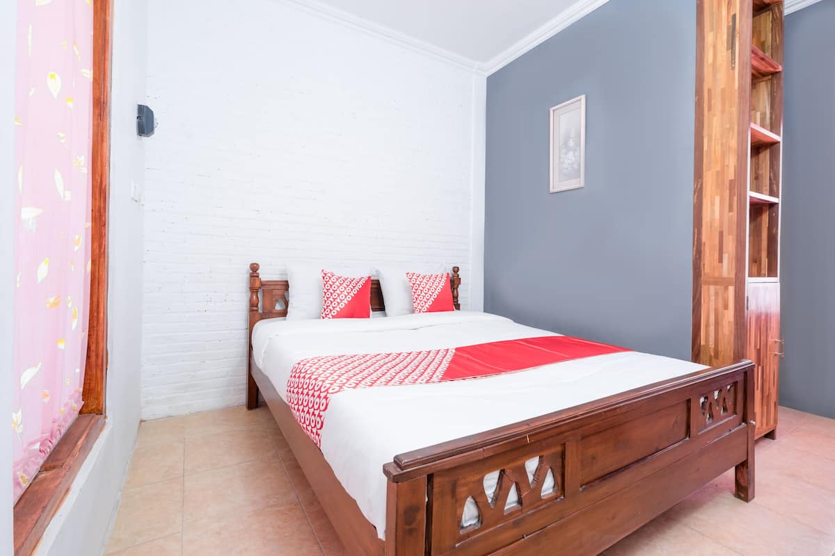 A bedroom with a wooden bed, white walls, a grey accent wall, and a pink curtain.