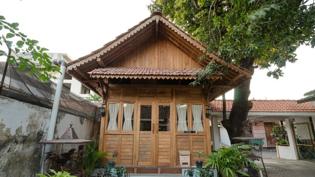 Une maison en bois avec un toit en tuiles, une porte d’entrée et un petit porche agrémenté de plantes en pot.
