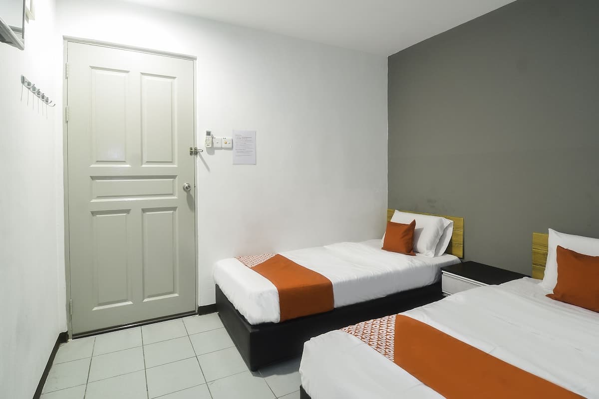 A hotel room with two beds, a door, a light switch, and a wall-mounted control panel.