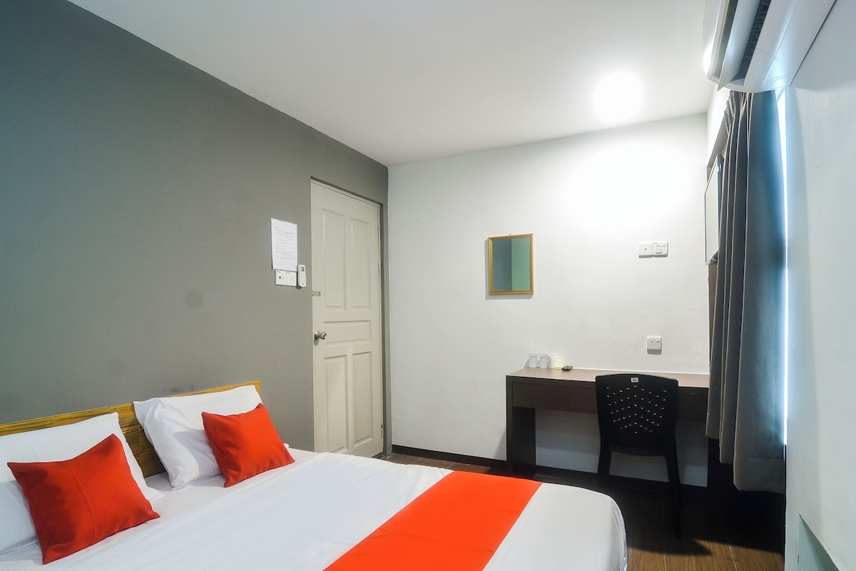 A hotel room with a bed, a desk, a chair, and a mirror.