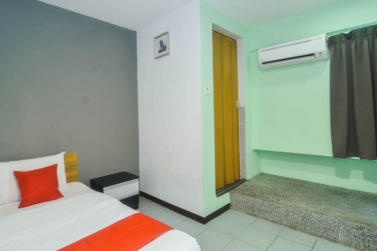 A hotel room with a bed, a nightstand, an air conditioning unit, and a door leading to another room.