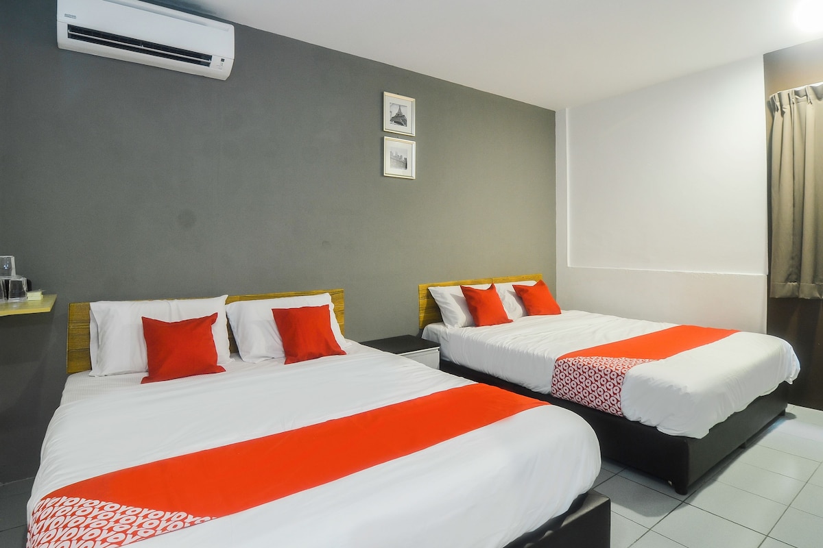 A hotel room with two beds, each with white bedding and orange accents, a grey wall, an air conditioning unit, and a framed picture.