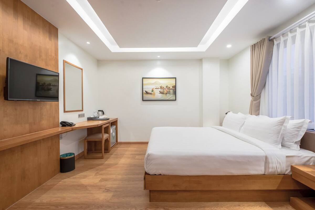 A modern hotel room with a bed, a desk, a chair, a TV, and artwork on the wall.