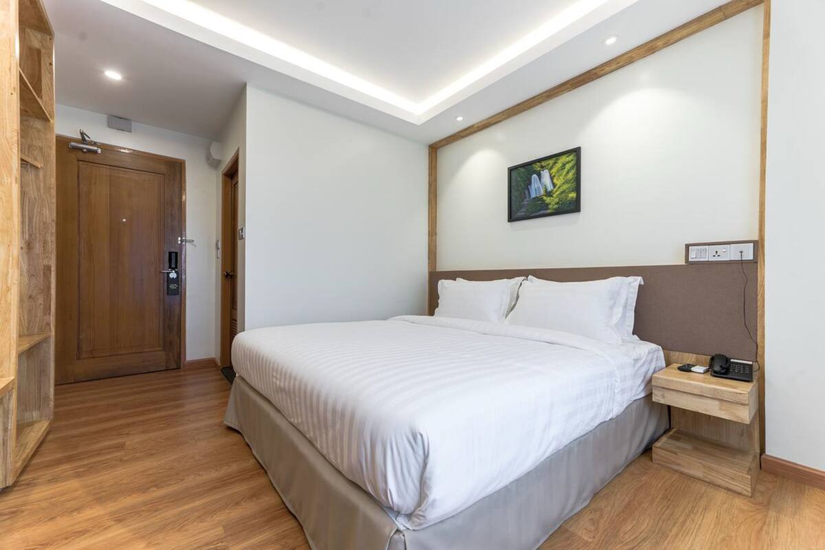 A hotel room with a large bed, a wooden headboard, a bedside table with a phone, and a painting on the wall.