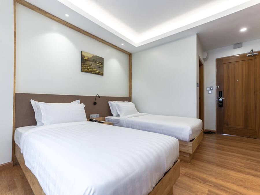Una habitación de hotel con dos camas individuales, cabecero de madera, un cuadro en la pared y un armario de madera.