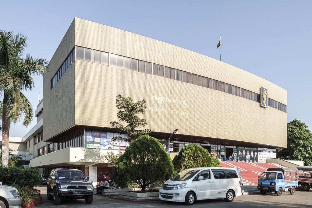 Un edificio con fachada de tejas, una bandera en la parte superior y una escalera que lleva a la entrada.