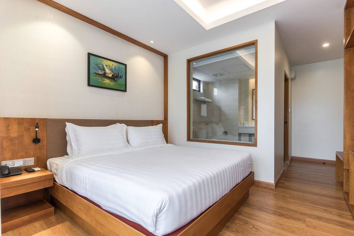 A modern hotel room with a large bed, wooden headboard, a bedside table with a phone, and a painting on the wall.