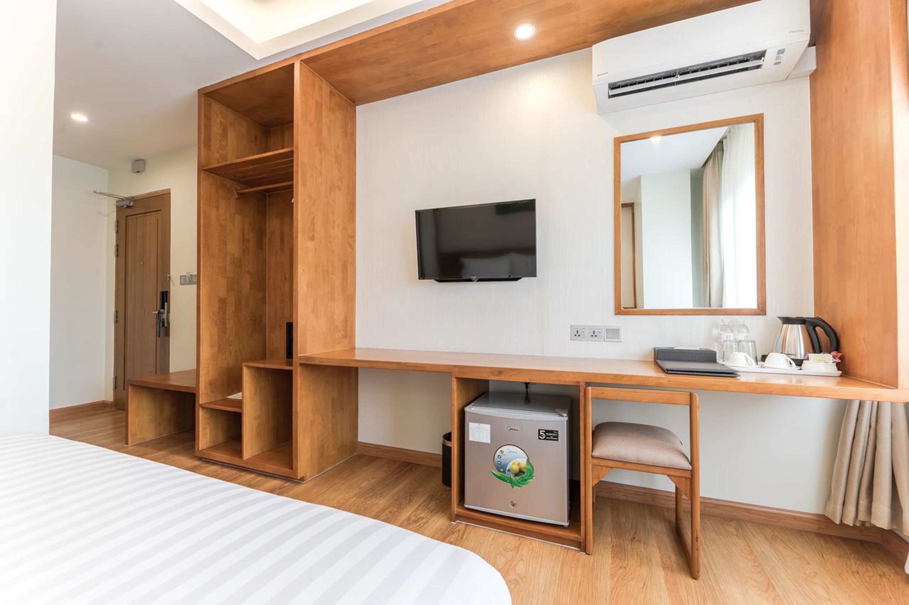 Een hotelkamer met een houten bureau, een televisie, een kleine koelkast en een bed.