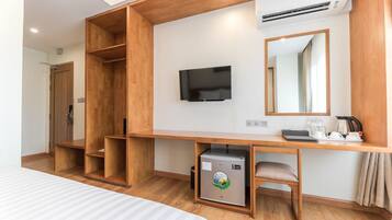 Een hotelkamer met een houten bureau, een televisie, een kleine koelkast en een bed.
