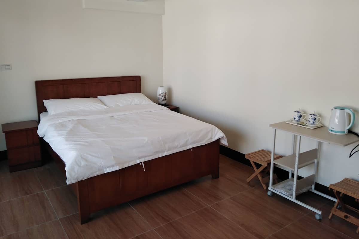 A neatly made bed with white linens, a wooden headboard, a bedside table with a lamp, and a small table with a kettle and teacups.