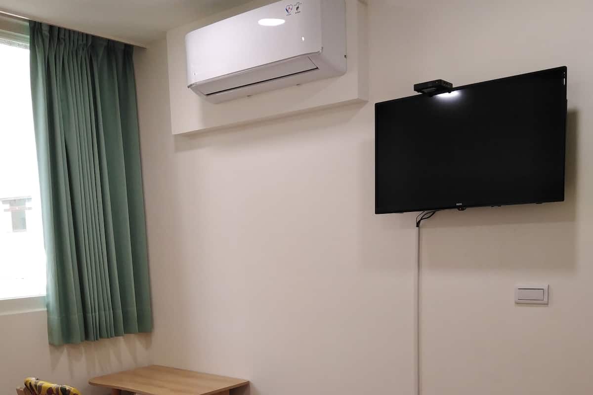 A hotel room with a bed, a desk, a chair, an air conditioner, a television, and a waste bin.