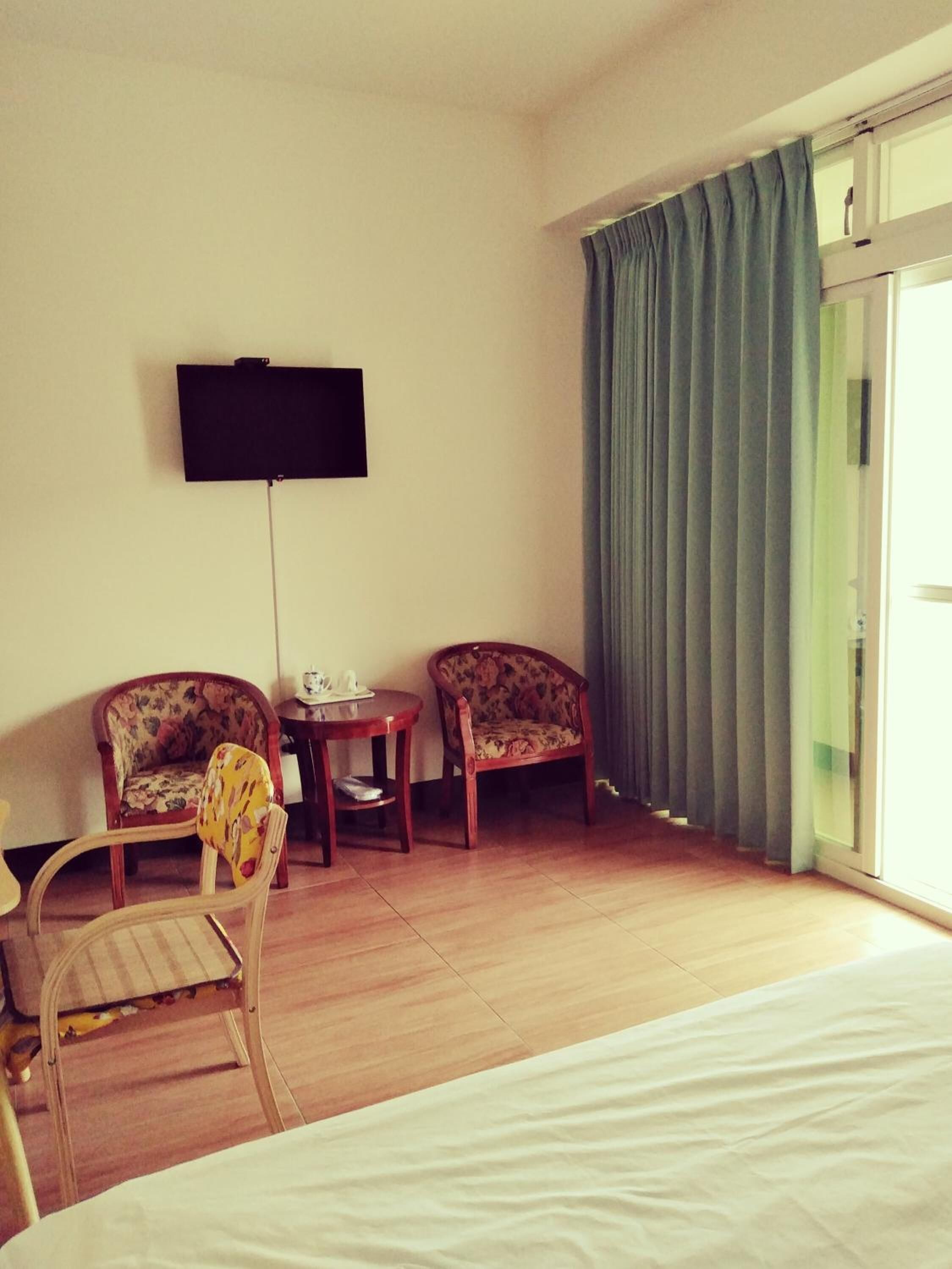 Une chambre d’hôtel comprenant un lit, deux fauteuils, une petite table, un téléviseur à écran plat fixé au mur et une grande fenêtre avec des rideaux.