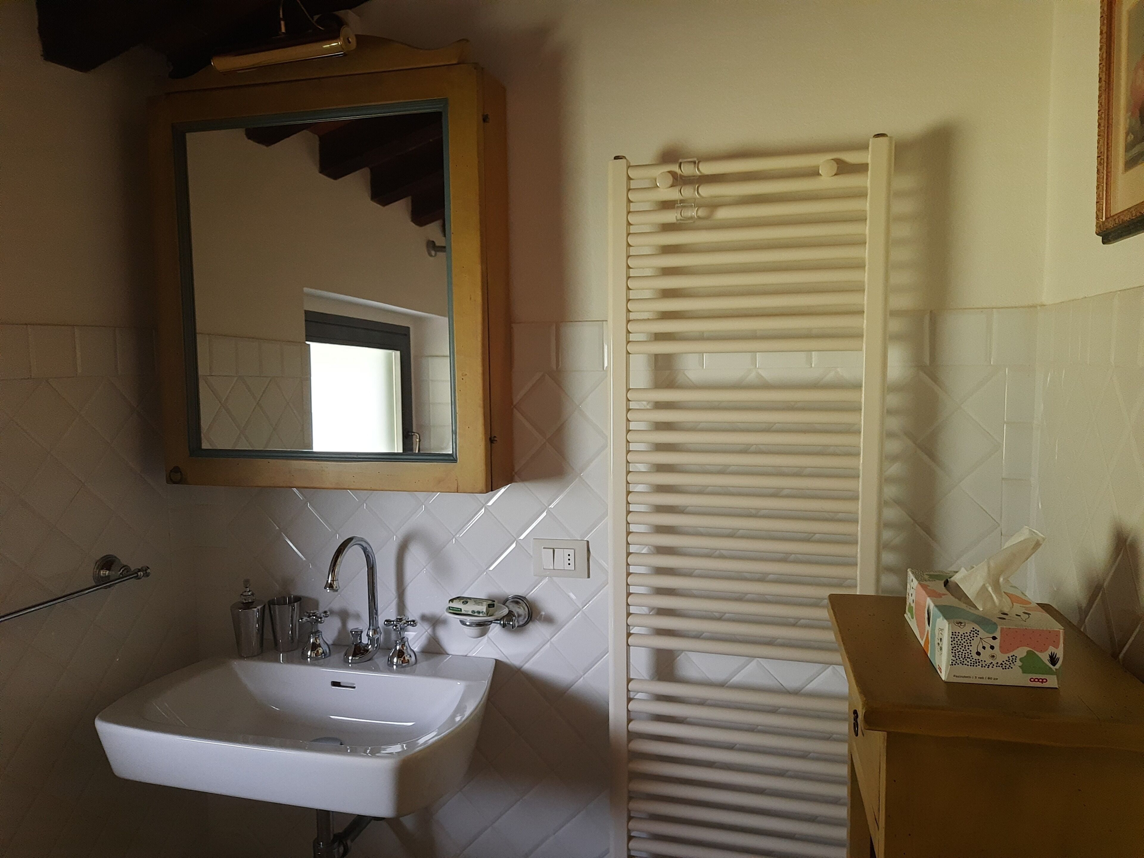 A bathroom with a white sink, a mirror, a towel rack, and a box of tissues on a wooden table.
