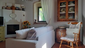 Ett mysigt vardagsrum med en soffa, en gungstol i trä, en tv och ett skåp med porslin.