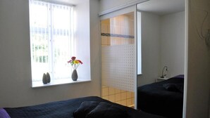 A bedroom with two beds, a window with a vase of flowers, and a sliding door leading to another room.