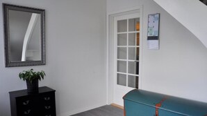 A room with a black dresser, a teal chest of drawers, a mirror, and a door with frosted glass panels.