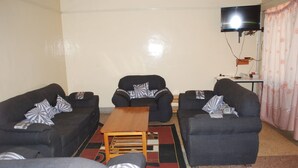 A living room with two sofas, a coffee table, and a flat-screen TV mounted on the wall. - The REE (Thika)