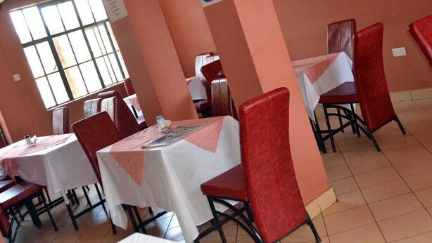 A dining area with tables and chairs, a sign indicating free Wi-Fi, and a window with bars. - The REE (Thika)