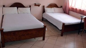 A bedroom with two wooden beds, a small shelf, and a window with curtains. - The REE (Thika)