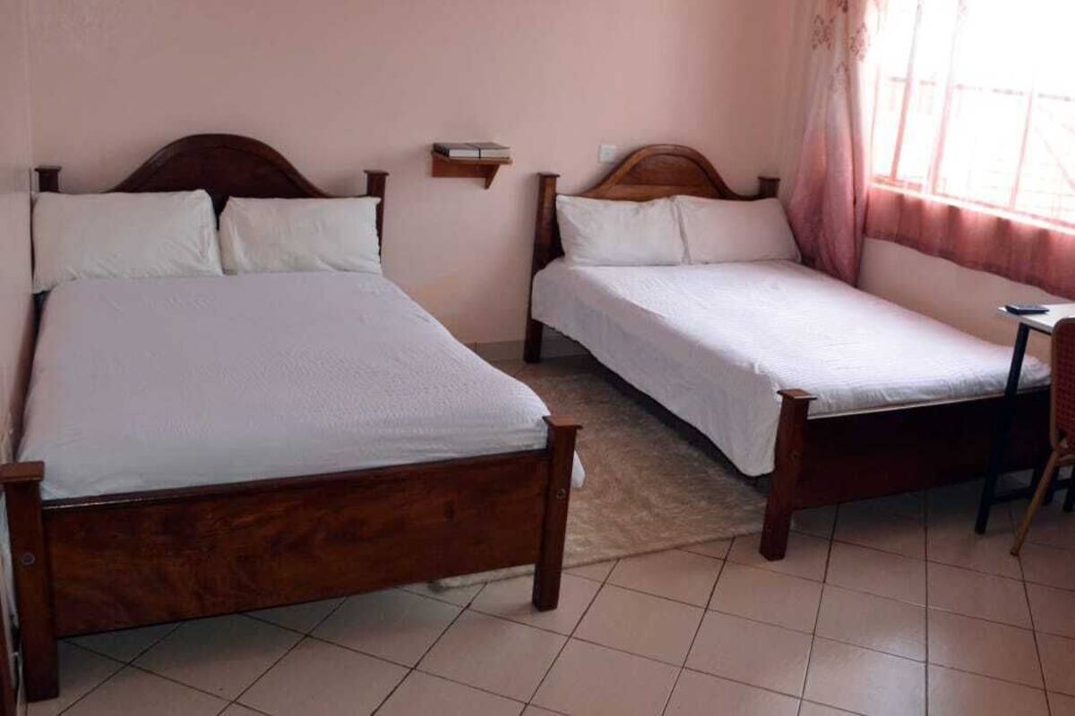 Un dormitorio con dos camas de madera, un estante pequeño y una ventana con cortinas.