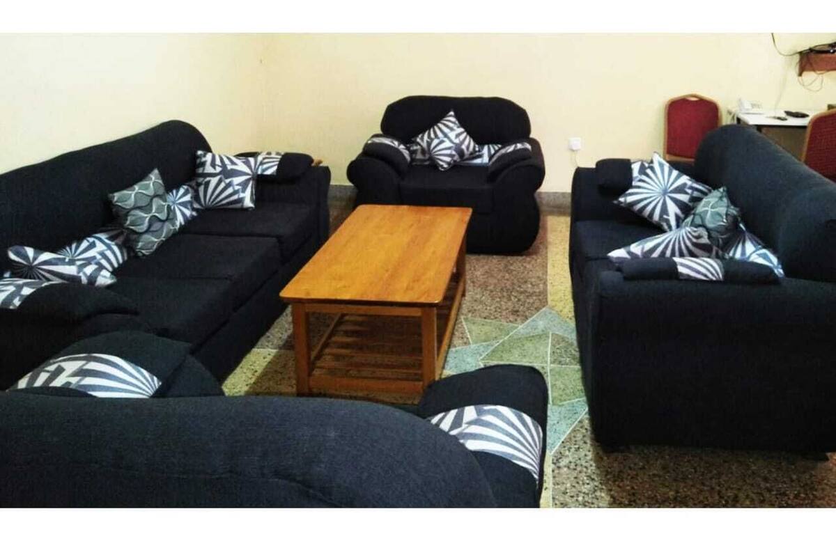 Una sala de estar con cuatro sofás negros, cada uno con cojines estampados, y una mesa de centro de madera en el medio.
