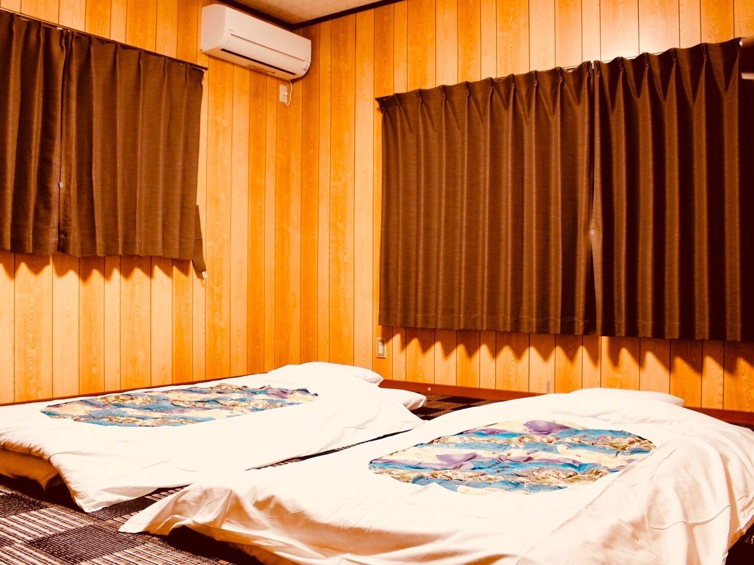 A room with two beds, wooden walls, and an air conditioning unit.