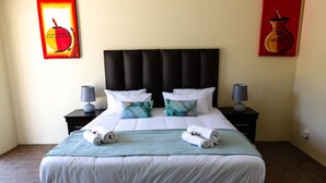 A neatly made bed with white linens and two rolled towels, a black upholstered headboard, and two bedside tables with lamps. - Avela (Magaliesberg)