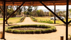 A covered walkway with a circular garden, leading to a park area with cars parked nearby. - Avela (Magaliesberg)