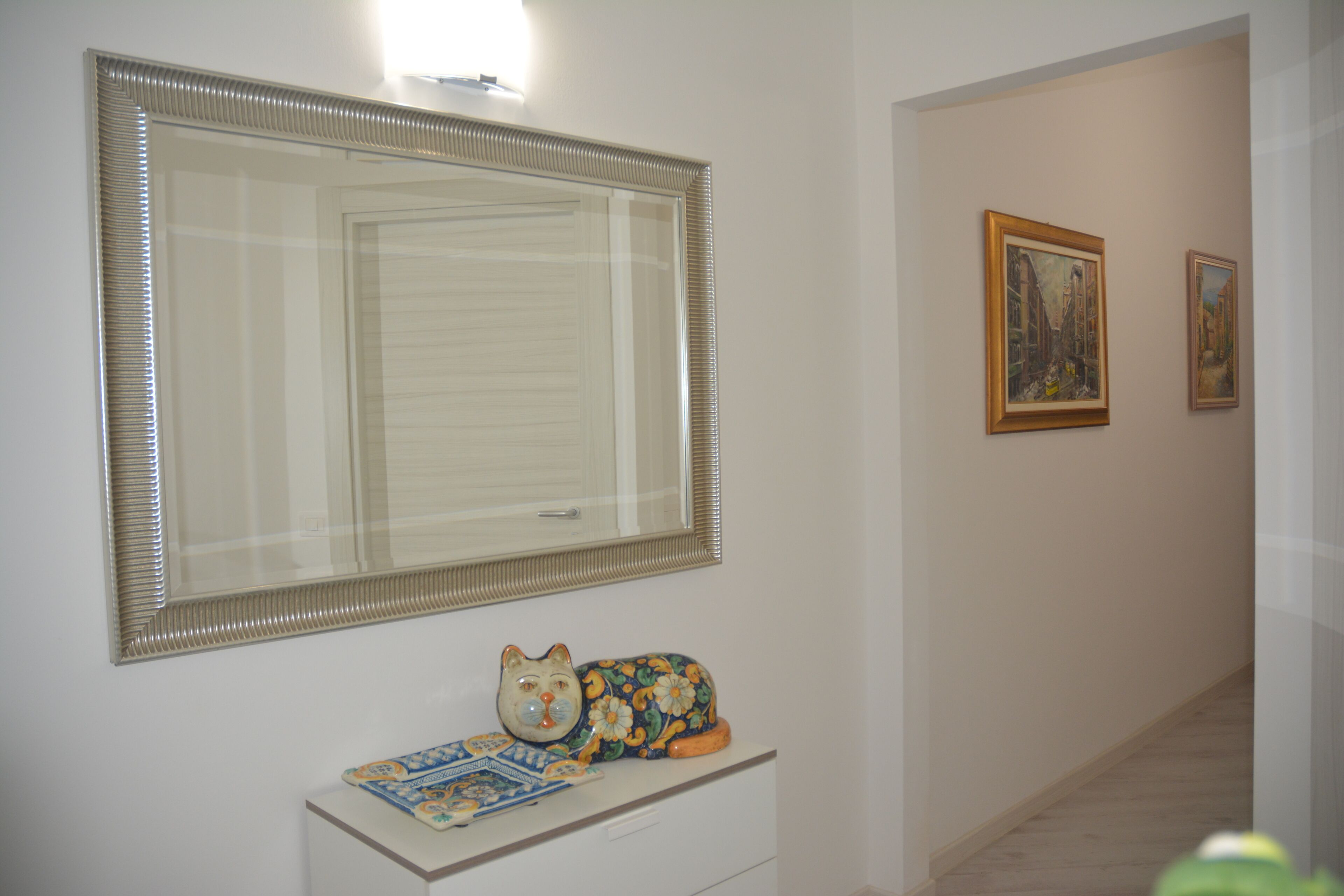 A hallway with a large mirror, a decorative cat statue, and two framed artworks on the wall.
