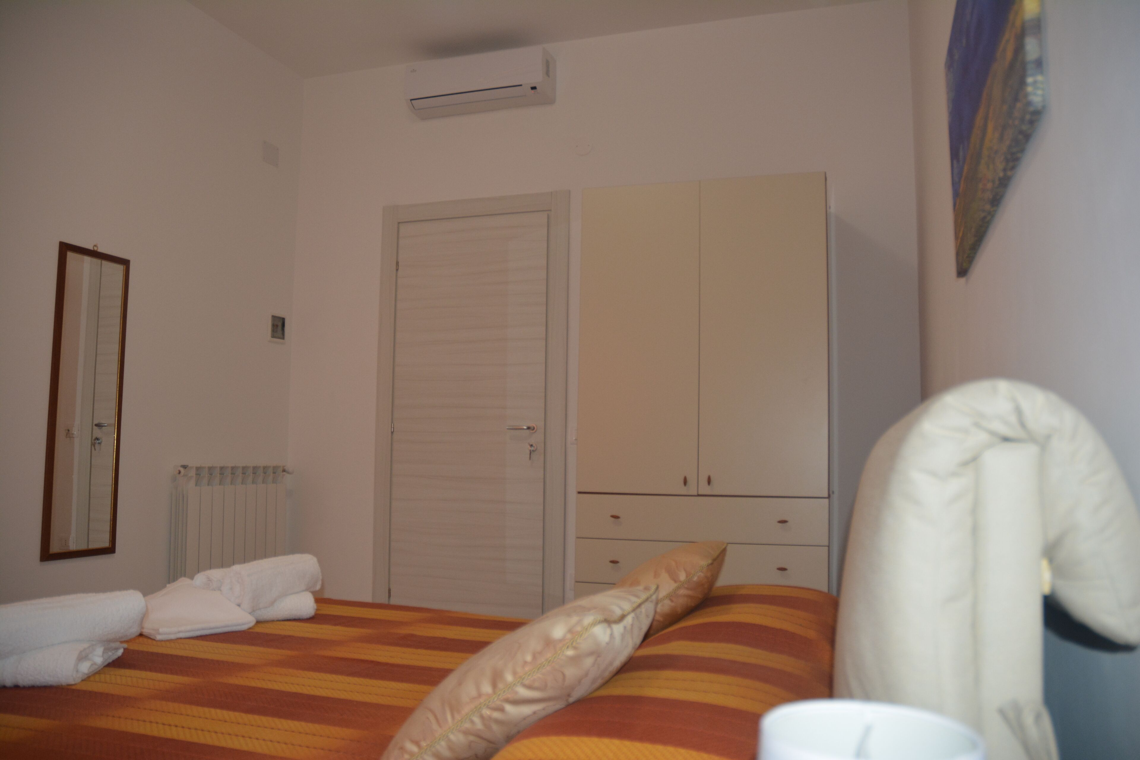 Un dormitorio con cama, armario, radiador y espejo.