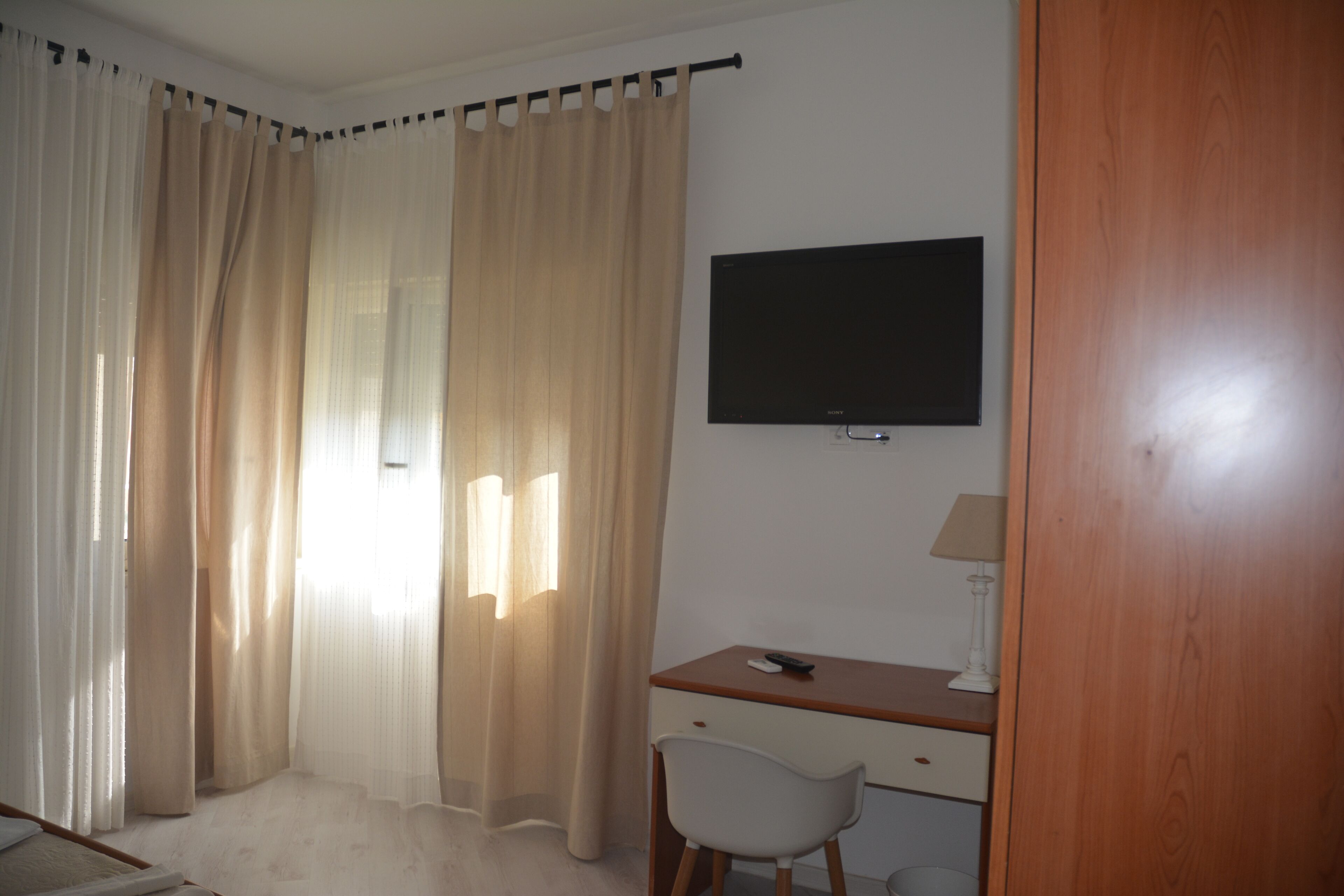 A bedroom with a bed, a desk with a chair, a TV, and a lamp.
