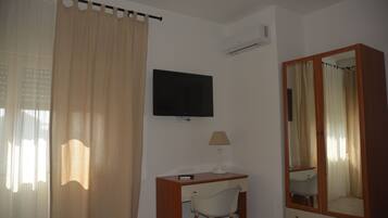 A hotel room with a bed, a desk with a chair, a television, a mirror, and a window with curtains.