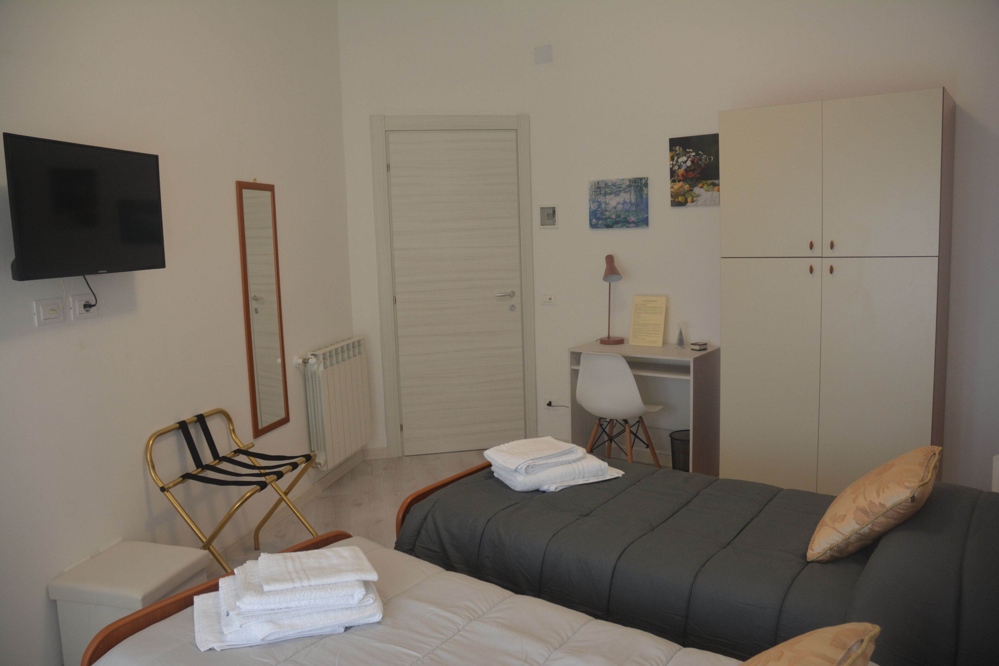 A bedroom with two beds, a desk, a chair, a TV, and a wardrobe.